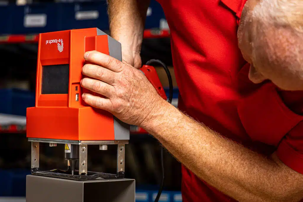 Operatore al lavoro con la macchina di marcatura portatile E-TOUCH XL, dotata di touch screen integrato, per eseguire incisioni precise direttamente su componenti metallici in officina.